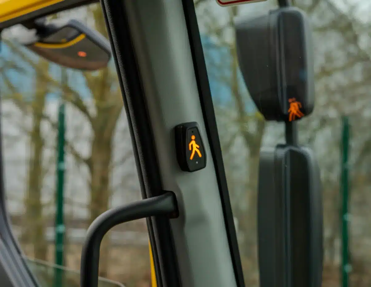 Close-up of a pedestrian detection warning indicator inside a vehicle, with a reflection of the alert on the side mirror.
