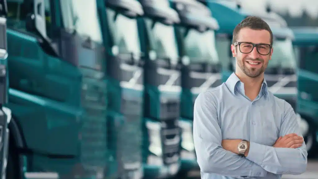 Smiling transport manager standing in front of fleet trucks after receiving expert installation service from Nationwide Fleet Installations