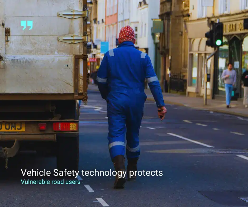 A man in high-visibility workwear walks behind a large commercial vehicle on a UK city street, highlighting the importance of vehicle safety technology for protecting vulnerable road users.