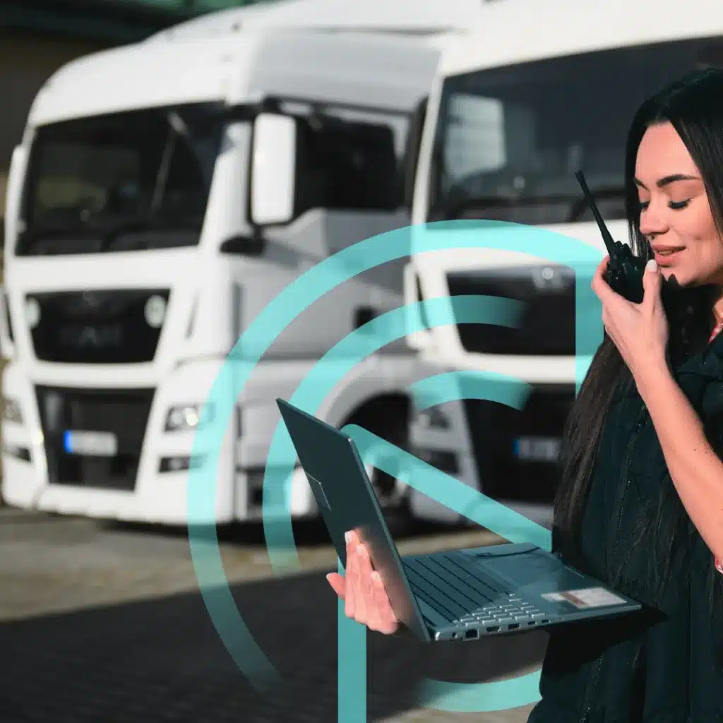fFleet operator using a laptop and radio to manage connected mobility and video telematics data with trucks in the background.