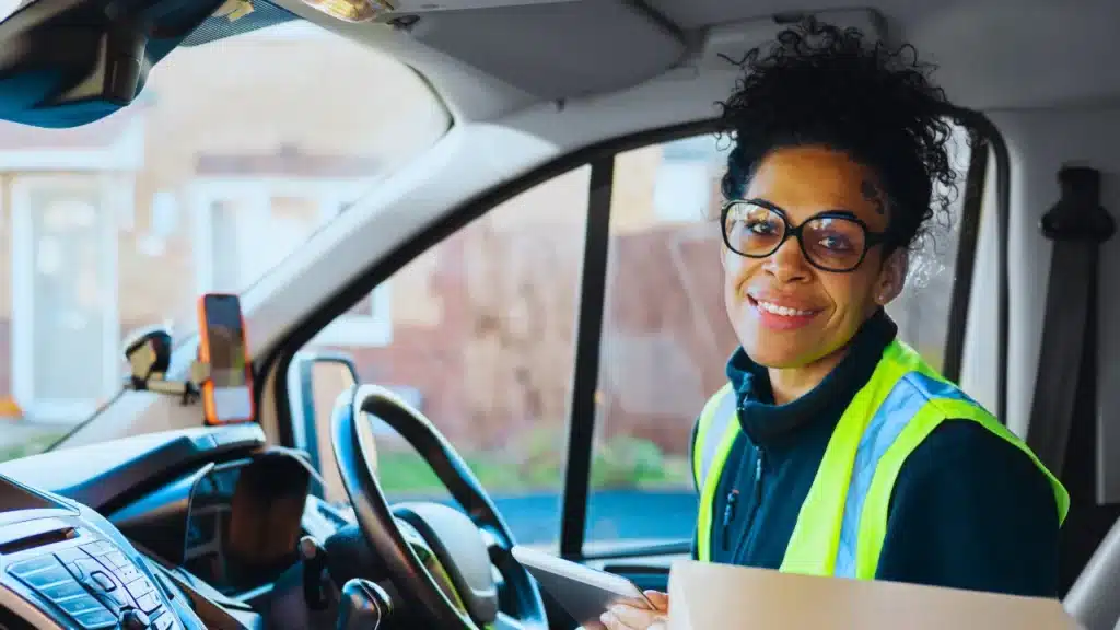 Female van driver wearing a high-vis vest, smiling while seated in her vehicle.